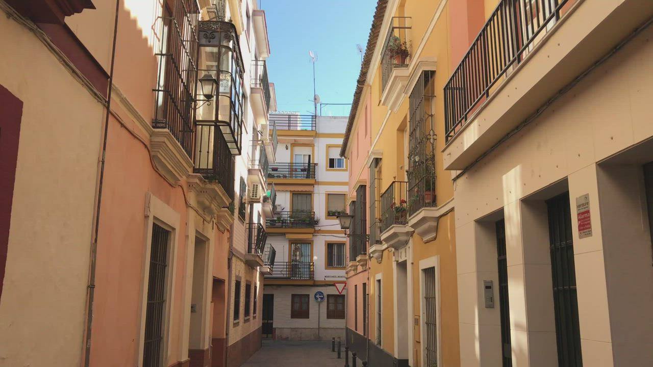 Una calle estrecha de edificios ocres y balcones de hierro en Sevilla